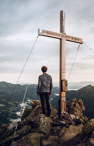 Ein Mann steht am Gipfelkreuz eines Berges in Gastein und blickt in das weite Gasteinertal